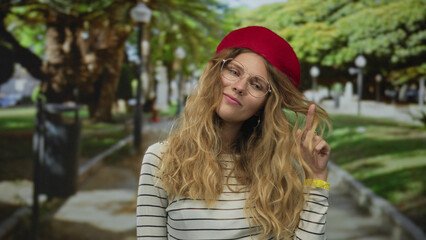 Confident woman hair gently tousled, smiling in a park with blonde beret, glasses and red striped...