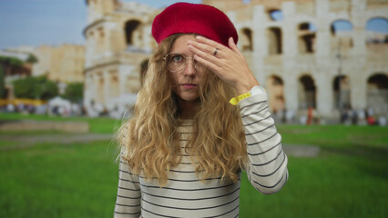 Woman uses hand covering eyes in italy, as blonde young beret and glasses style highlights...