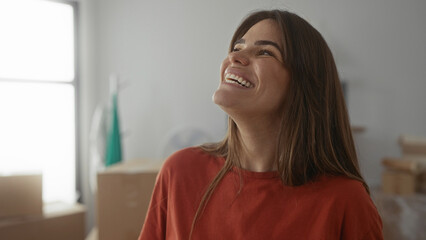 Young hispanic woman smiling joyfully in her new apartment surrounded by moving boxes, capturing...