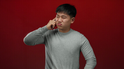 Young man speaking on phone in front of a red background conveying an emotional connection with...