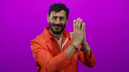 Hispanic man in orange jumpsuit with handcuffs stands against a vivid purple background, exuding emotion.