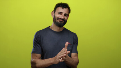 Hispanic man with beard clapping against a vibrant yellow background and smiling, suggesting...