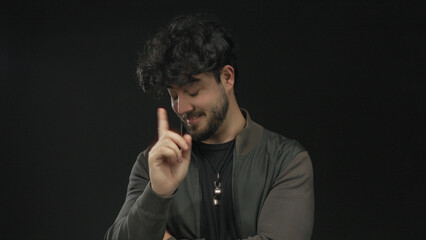 Young man with beard and curly hair gestures expressively against a black background, showcasing a...