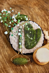 delicate cosmetic composition with gypsophila, quartz roller, gua sha, face wash brush and facial care sponge on wooden background vertical, creative focus