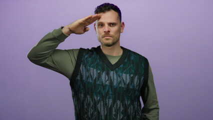 Obraz premium Man saluting against a purple background, wearing a green sweater, displaying confidence and focus, expressing strength and style with a direct gaze, isolated and composed.