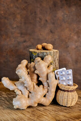 still life with a large ginger root and a wicker vase with silver convales with tablets, a tree stump and three nuts on a wooden background, close-up