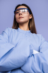 A stylish individual wearing protective eyewear and a uniform stands confidently against a solid backdrop, exuding professionalism and a modern aesthetic in a minimalist setting.