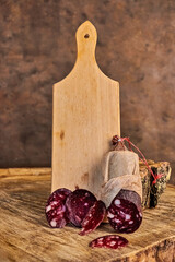 Raw smoked sausage in a fabric casing and sliced ​​pieces against the background of a long wooden cutting board. The concept of traditional gastronomy, meat delicacies and snacks.