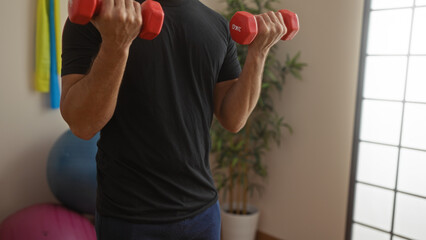 Man lifting weights indoors at gym with dumbbells, focusing on exercise and strength in an athletic...