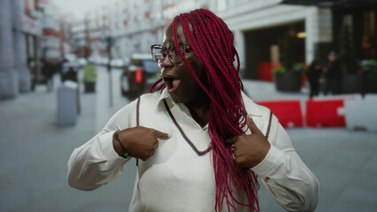 African american woman with surprise expression gestures to herself on a bustling city street,...
