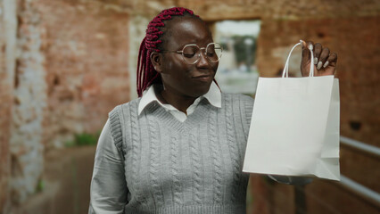 Woman smiling and examining a white shopping bag indoors at a construction site, showcasing her...