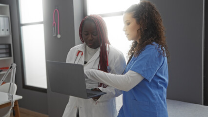 Obraz premium Women doctors discussing patient files on laptop in modern clinic workplace highlighting healthcare teamwork and diversity.