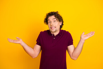 Confused young man shrugging against a vibrant yellow background, expressing uncertainty and humor...