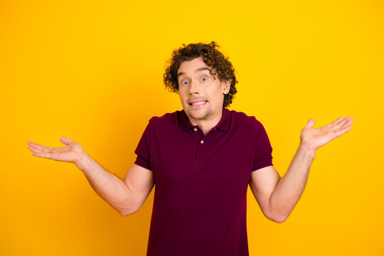 Confused young man shrugging against a vibrant yellow background, expressing uncertainty and humor in a casual outfit