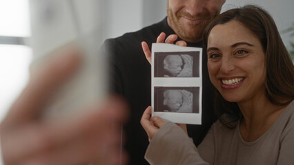 Couple joyfully taking selfie with ultrasound images in cozy home setting, highlighting excitement and anticipation of pregnancy journey together.
