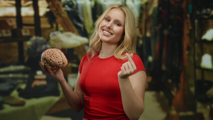 Woman in red shirt holding brain model with heart gesture in clothing store, blending science and fashion.