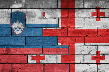 colourful painted big national flag of georgia and flag of slovenia on a massive old brick wall background. concept