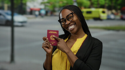 Fototapeta premium Woman smiling with greek passport on urban street, suggesting travel and identification in a city setting, prominently featuring an african woman in glasses outdoors.