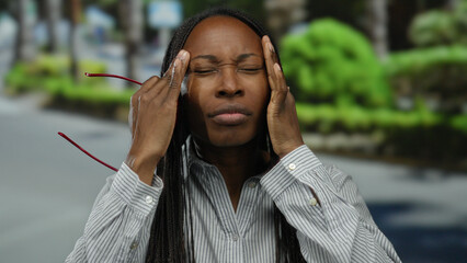 Woman in pain outdoors holds red glasses on city street wearing striped shirt under evening light