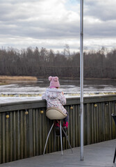 A child sits alone on a chair on a cafe terrace by the river.
