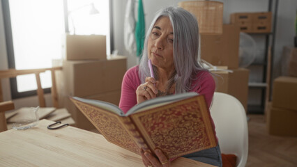 Senior woman reading in a new home surrounded by moving boxes, thinking and planning her new space filled with possibilities.