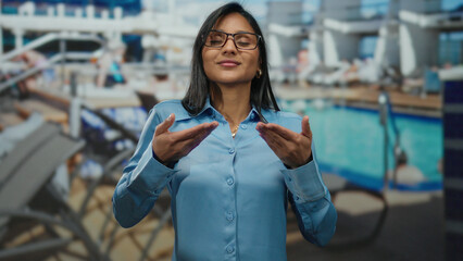 Young woman in blue shirt practicing breathing outdoors on a cruise ship, surrounded by a relaxed poolside atmosphere, capturing a moment of tranquil meditation.