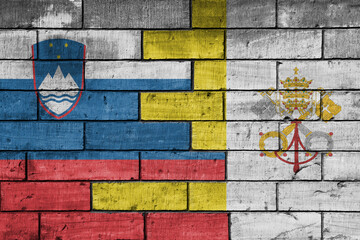 colourful painted big national flag of vatican city and flag of slovenia on a massive old brick wall background. concept