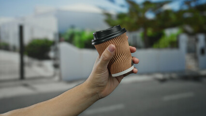 Man holding a coffee cup on a quiet city street with a blurred suburban background in a peaceful...