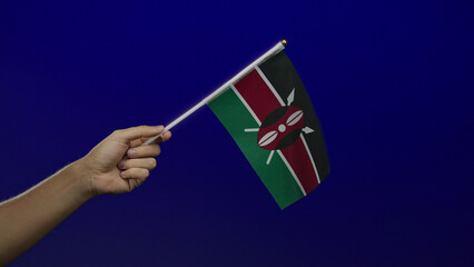 Caucasian man holding a small kenyan flag against an isolated blue wall background.