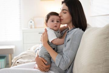 Obraz premium Mother kissing her cute baby on sofa at home. Space for text