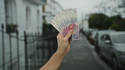 Man holding argentine pesos on a city street, showcasing the vibrant banknotes against a blurred...