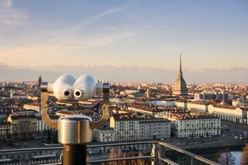 Public binoculars capture panoramic sunset view of Turin, Italy with Mole Antonelliana and Alpine backdrop. Elevated urban vista in the heart of Piedmont region