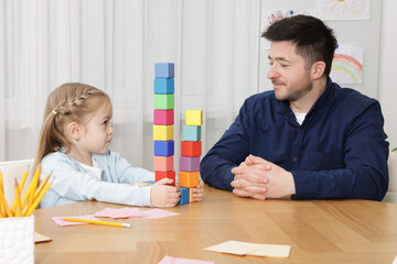 Teacher and little girl with colorful cubes at desk indoors