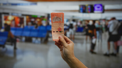 Hand holding malaysian ringgits in an airport terminal, highlighting travel, finance, and international currency context, surrounded by people boarding a plane indoors.