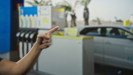 Man pointing finger near petrol station with fuel pumps and vehicle in background outdoors in sunny area with clear sky indicating directions or actions towards destination