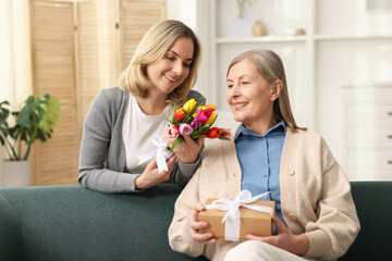Smiling daughter congratulating her mom with bouquet of tulips and gift at home. Happy Mother's Day