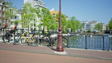 Fototapeta premium Blurred view of amsterdam canal with bicycles against a bokeh background of trees and buildings on a sunny day.
