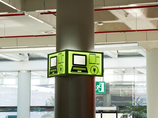 Green illuminated sign on a pillar displaying computer and device icons in a modern airport terminal
