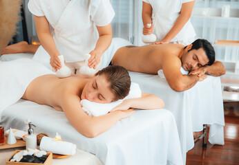 Obraz premium Hot herbal ball spa massage body treatment, masseur gently compresses herb bag on couple customer body. Tranquil and serenity of aromatherapy recreation in day lighting ambient at spa salon. Quiescent