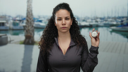 Woman holding stopwatch at seaside port, wearing athletic attire, showcasing determination and...