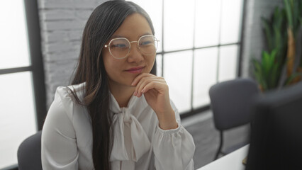 Obraz premium Woman working in modern office environment, displaying focus and professionalism, captures contemporary interior with natural lighting and greenery, evoking productivity and determination.