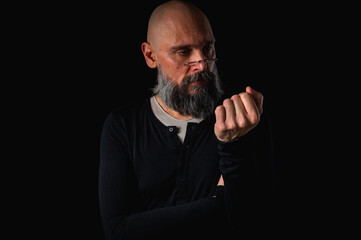 Portrait of a cunning-looking bald man with gray beard and glasses, clasping hands. Dark background. Mischievous or scheming expression. Concept of plotting, sarcasm, or ironic humor