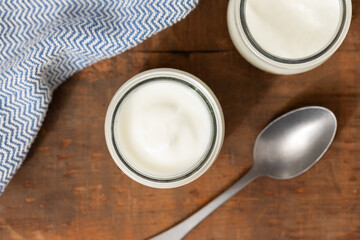 Top view of glass jars of yogurt, wooden table, spoon, and blue cloth.