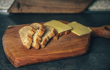 Slices of fresh bread and cheese arranged on a wooden cutting board in a cozy kitchen setting. Natural light enhances the warm, homemade atmosphere. A simple yet appetizing composition that captures