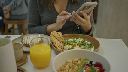 Woman enjoying breakfast in modern restaurant capturing meal with phone vibrant dishes and fresh orange juice create luxury brunch scene indoors