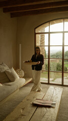 Woman placing lemons in a basket indoors in a mediterranean style house with wooden beams and stone walls, wearing glasses, creating a warm and rustic atmosphere.
