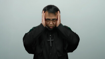 Asian man in priest attire holding head in distress against plain background, conveying emotion and...