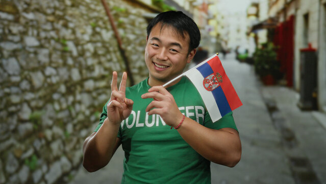 Young man wearing green shirt holding serbian flag in urban street, symbolizing cultural pride and volunteer spirit outdoors. - Powered by Adobe
