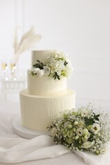 Delicious wedding cake with floral decor and bouquet on table indoors