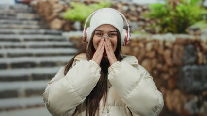 Woman smiling outdoors with headphones and winter jacket on street steps background showcasing...